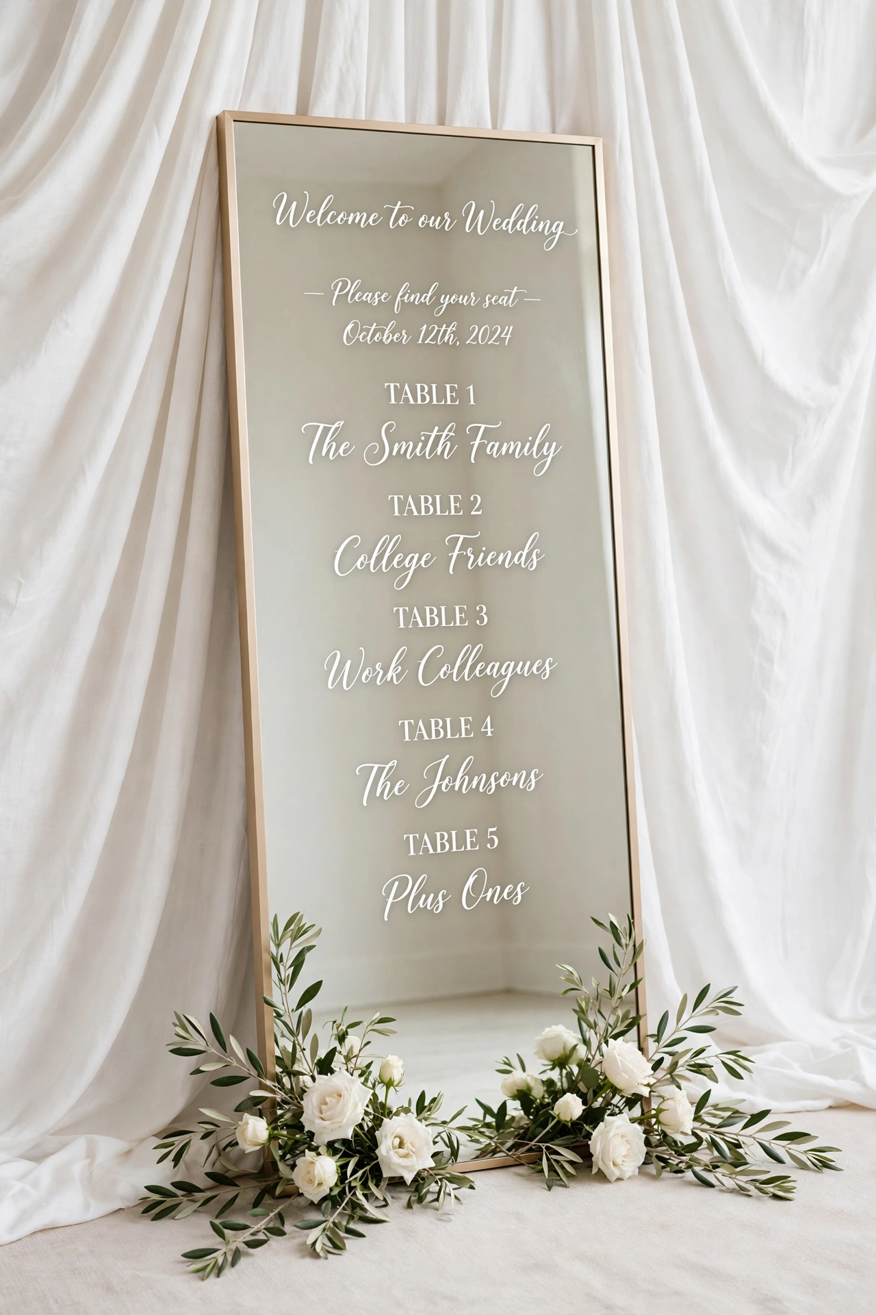 Floor-length champagne-frame mirror wedding seating chart leaning against white draped fabric with white roses and olive branches