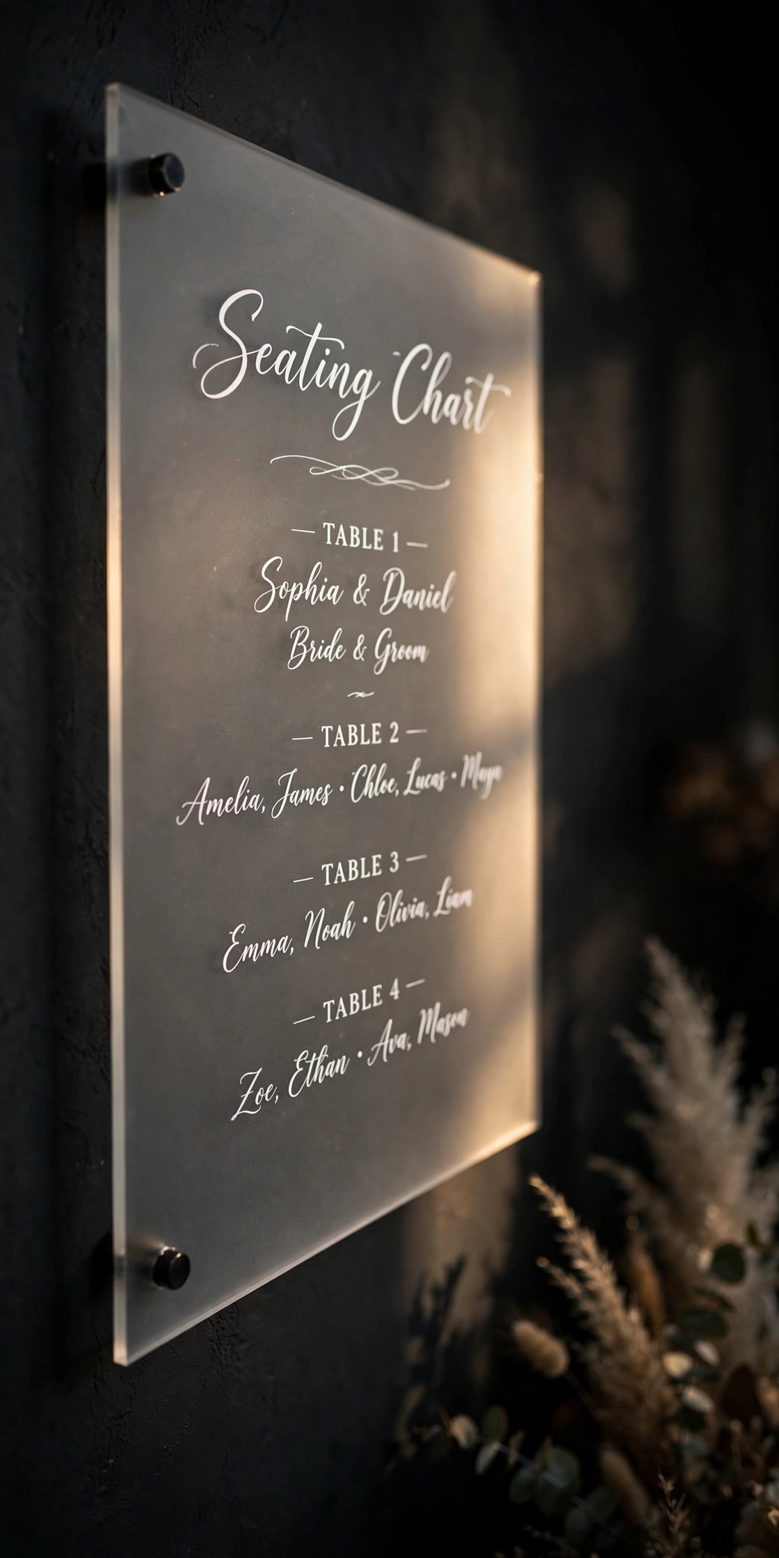 Frosted acrylic wedding seating chart panel with modern white calligraphy on a dark moody wall